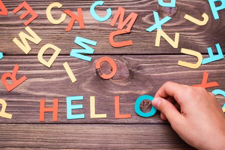 Children`s hands make up the word "hello" from colored carved cardboard letters on a wooden background. Top viewの写真素材