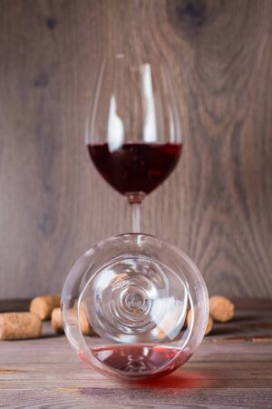 One glass with the remains of red wine is lying, the other is standing filled with red wine behind on a wooden tableの写真素材