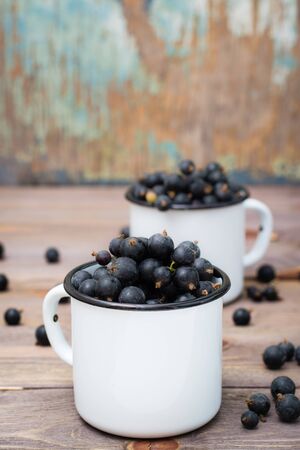 Ripe black currants in metal white mugs on a wooden table. Rustic styleの写真素材