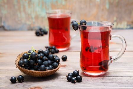 Fresh ripe black currant compote in a glass and a bowl of berries on a wooden tableの写真素材
