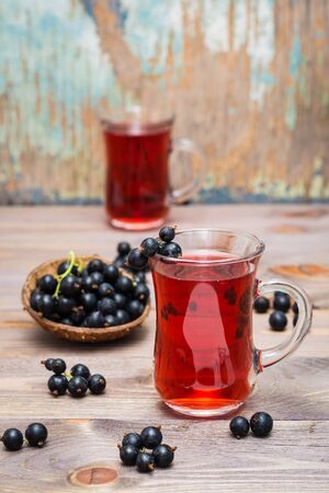 Fresh ripe black currant compote in a glass and a bowl of berries on a wooden tableの写真素材