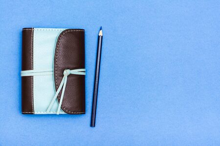 Closed organizer in a two-color leather binding and a pencil on a blue background. Top view. Copy...