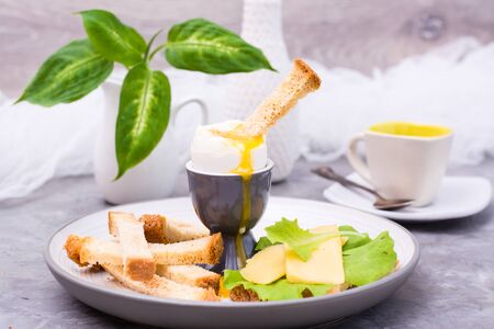 Soft boiled chicken egg, crackers, pieces of cheese and lettuce on a plate on the table. Ready to...