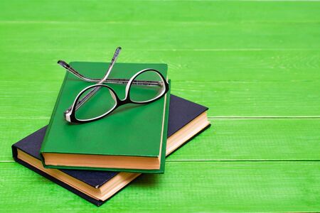 Two hardcover books and glasses  on a green wooden table. Copy space