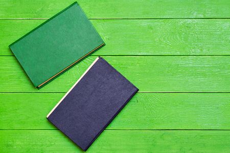 Two hardcover books on a green wooden background. Top view