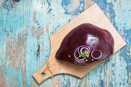 A piece of raw beef liver on a cutting board, onion and spices for cooking on a wooden table. Top viewの写真素材