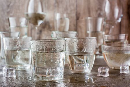 Many glasses of water splashed with drops and pieces of ice on a gray table