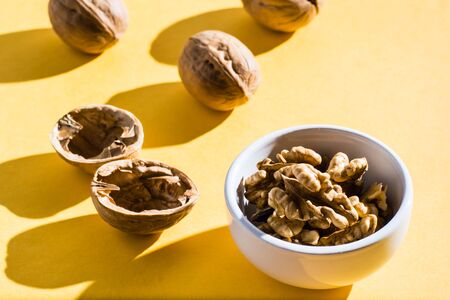 Walnut kernels in a bowl and walnut shells on a yellow table.  Hard lightの写真素材