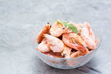 Group of frozen shrimp and a leaf of arugula in a glass bowl on a gray tableの写真素材