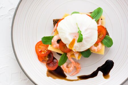 Appetizing bruschetta on rye bread with poached egg, tomato, shrimp and arugula on a plate. Top viewの写真素材