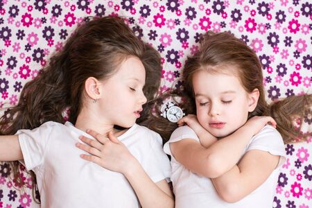 Two sleeping girls and a white alarm clock in between. Top viewの写真素材