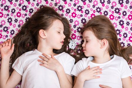 Two sleeping girls and a white alarm clock in between. Top viewの写真素材