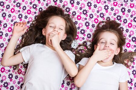 Two waking up yawning girls and an alarm clock in between. Top viewの写真素材