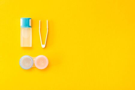 Accessories for storing lenses: a bottle of liquid, container and tweezers on a yellow background. Top viewの写真素材