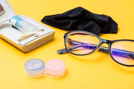 Accessories for storing lenses: container, a bottle of liquid and tweezers in a case, glasses and cloth on a yellow background. Concept - glasses against lensesの写真素材