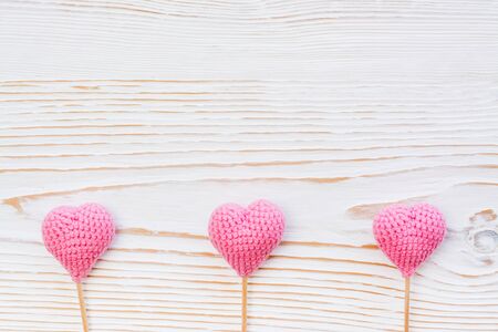 Three pink knitted hearts on sticks on a white wooden backgroundの写真素材
