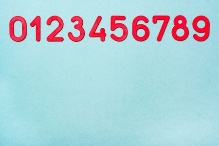 Red plastic numbers from zero to nine lie in a row on a green background. Top View. Copy space