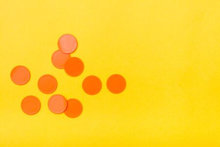 Orange plastic flat circles lie chaotically on a yellow background. Copy spaceの写真素材