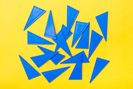 Blue plastic flat triangles are scattered chaotically on a yellow background. Top Viewの写真素材