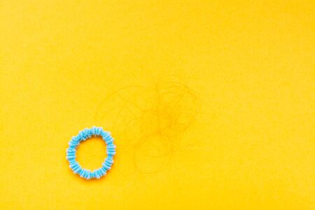 Band for hair and hanks of fallen hair on a yellow background. Concept - hair loss. Top Viewの写真素材