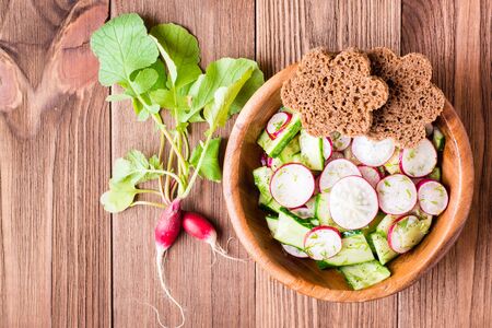 Lenten spring vegetable salad of cucumber, radish, greens and rye bread  in a plate on a wooden table. Top viewの写真素材