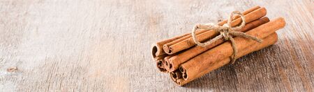 Cinnamon sticks, tied with a rope, lie on a wooden table. Fresh spice