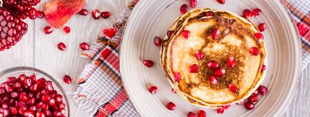 A pile of pancakes with pomegranate seeds on a plate. Top view