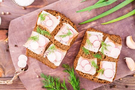 Sandwiches from rye bread, salted bacon, radish and dill on a cutting board on a wooden table. Top viewの写真素材