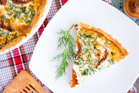 Slice of homemade french quiche pie with tomato, cheese and herb on a plate. Top viewの写真素材