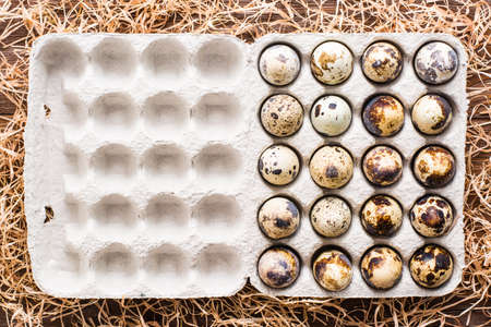 Quail eggs in a box and straw on a wooden table. Top view