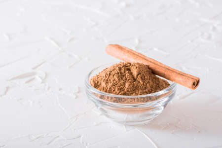 A stick of cinnamon lies on a bowl of ground cinnamon on the table