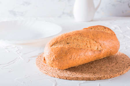 Fresh baguette with bran on a cork substrate on a white table. Crisp bread ready to eatの写真素材