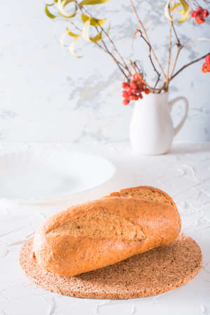 Fresh baguette with bran on a cork substrate on a white table. Crisp bread ready to eatの写真素材