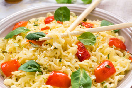 Close up of noodles with pepper, lettuce leaves and sesame seeds in a plate and chopsticksの写真素材