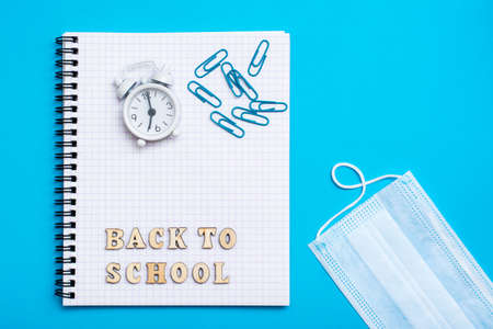 Back to school. Social distancing. Alarm clock, wooden letters, paper clips on a notebook,...