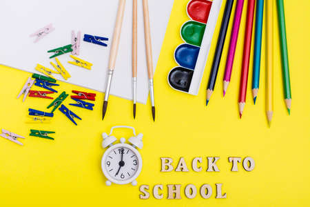 Back to school. Painting supplies, alarm clock and inscription in wooden letters on a yellow...