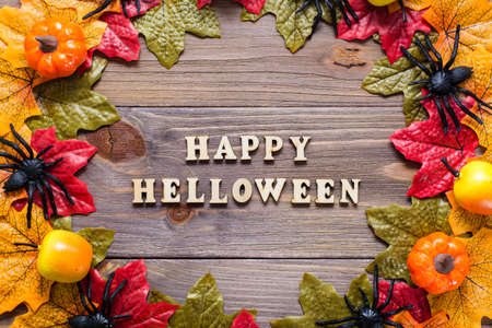 Halloween happy congratulations. Phrase lettering in a circle of maple leaves, spiders, pumpkins and apples on wooden backgroundの写真素材