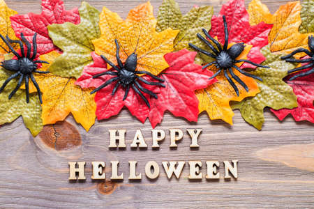 Halloween happy. Phrase lettering surrounded by maple leaves and spiders on wooden background