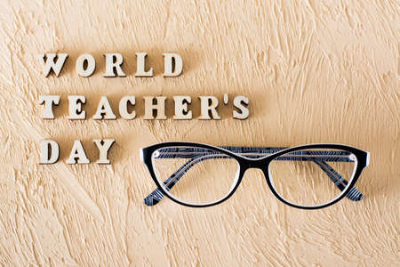 World Teachers Day. Text from wooden letters and glasses on a textured beige plaster background