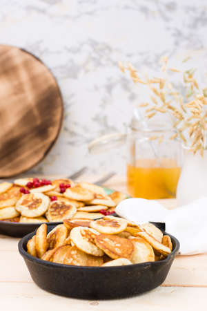 Trend breakfast. Dutch mini pancakes in a pan and on a plate with red currants and honey on a wooden...