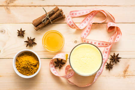 Detox drink. Golden milk with turmeric and cinnamon in glasses and a measuring tape on a wooden table. Slimming concept. Top viewの写真素材