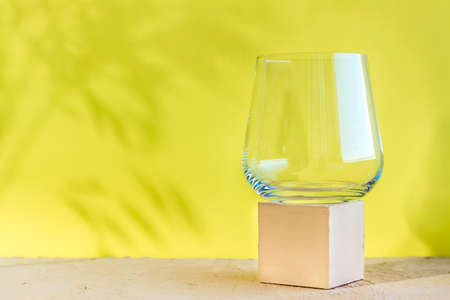 Mockup. Empty transparent glass on a textured cube on a beige surface on a yellow background with shadows from plantsの写真素材