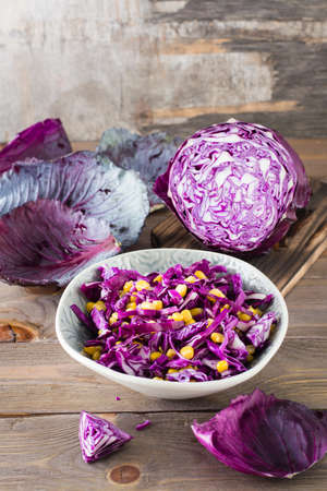 Red cabbage salad with corn grains in a plate on a wooden table. Vegetarian food. Vertical viewの写真素材
