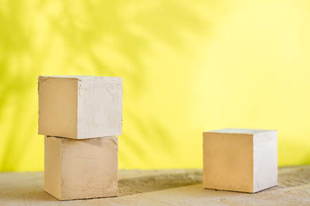Mockup. Three textured cubes on a beige surface on a yellow background with plant shadows.の写真素材