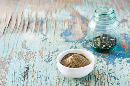 Black ground pepper in a white bowl and a can of peppercorn on an old wooden table. Spice to improve...
