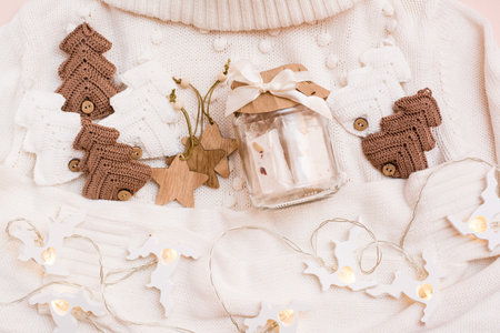 Christmas mood. Jar with paste, knitted fir-trees, wooden toys and a garland of deer on a white sweater. Handicraft decor. Zero waste. Top viewの写真素材