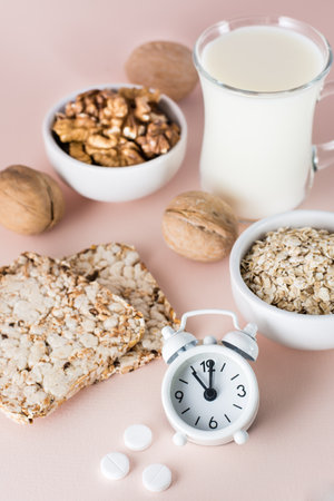 Good sleep. Foods for good sleep - milk, walnuts, crispbread, oatmeal, sleeping pill and alarm clock on pink background. Vertical viewの写真素材