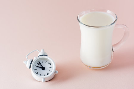 Good sleep. A glass of milk a product for good falling asleep and an alarm clock on a pink background. Evening ritualの写真素材