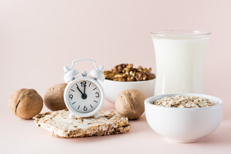 Good sleep. Alarm clock on the background of products for good falling asleep - milk, walnuts, oatmeal crispbread on a pink backgroundの写真素材
