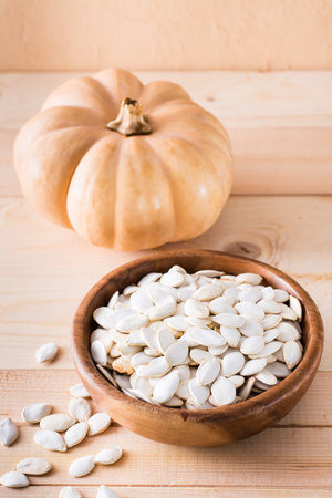 Roasted pumpkin seeds in a plate and pumpkin on a wooden table. Vertical viewの写真素材